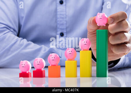 Close-up di un imprenditore la mano collocando Salvadanaio sulla sommità del multi colore grafico di Business Foto Stock