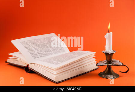 Candela in candeliere e aprire il vecchio libro isolato su sfondo arancione Foto Stock