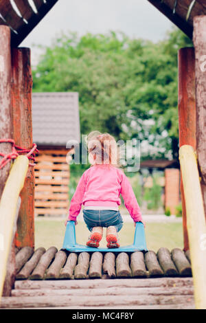 Poco toddler girl giocare nel parco giochi permanente sulla diapositiva Foto Stock