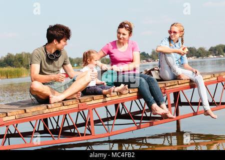 Famiglia spendere tempo di vacanza insieme avente uno snack seduti sul pontile sul lago sulla giornata di sole in estate. Tempo la famiglia di qualità di fine settimana Foto Stock