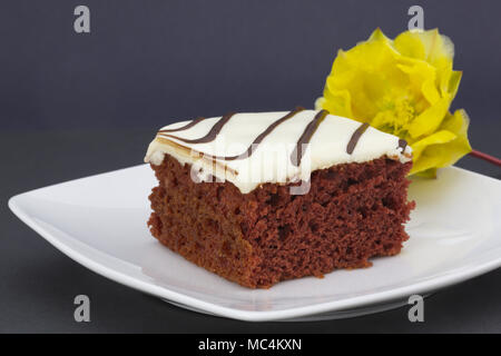 Square fetta di torta rossa del velluto con glassa bianca sul piatto. Giallo ficodindia blossom al lato sud-ovest aggiunge accento. Semplice, elegante, orizzontale p Foto Stock