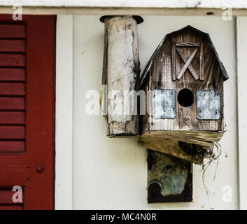 Un vecchio birdhouse attaccato ad un granaio. Ramoscelli da un nido all'interno della casa può essere visto cadere fuori il fondo. Foto Stock