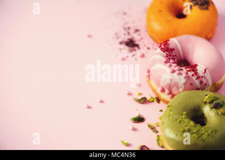 Ciambelle colorate con ciliegina sulla rosa pastello sfondo. Arancio dolce, verde, rosa ciambelle con pistacchio, cioccolato. Appartamento laico, vista dall'alto, spazio di copia Foto Stock