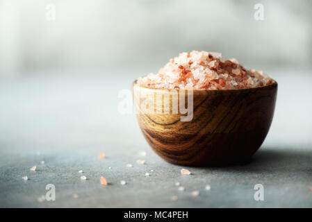 Rosa Sale Himalayano i cristalli e la polvere in ciotole di legno sul cemento grigio Sfondo. Dieta sana senza sale. Spazio di copia Foto Stock