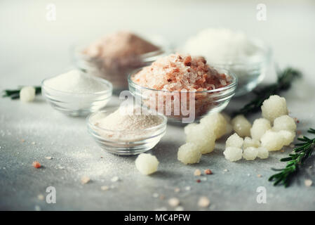 Mix di diversi tipi di sale sul cemento grigio Sfondo. Sali marini, nero e rosa himalayana di cristalli di sale, polvere, rosmarino. Sale le sfere di cristallo del Mar Morto. Spazio di copia Foto Stock