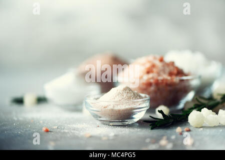 Mix di diversi tipi di sale sul cemento grigio Sfondo. Sali marini, nero e rosa himalayana di cristalli di sale, polvere, rosmarino. Sale le sfere di cristallo del Mar Morto. Spazio di copia Foto Stock