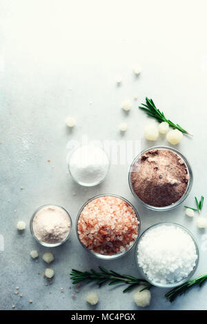 Mix di diversi tipi di sale sul cemento grigio Sfondo. Sali marini, nero e rosa himalayana di cristalli di sale, polvere, rosmarino. Sale le sfere di cristallo del Mar Morto. Copia dello spazio. Vista dall'alto. Foto Stock