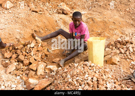 Lugazi, Uganda. Il 18 giugno 2017. Un ragazzo ugandese rocce di rottura in lastre di piccole dimensioni per il suo caposquadra. In sostanza il lavoro minorile. Foto Stock