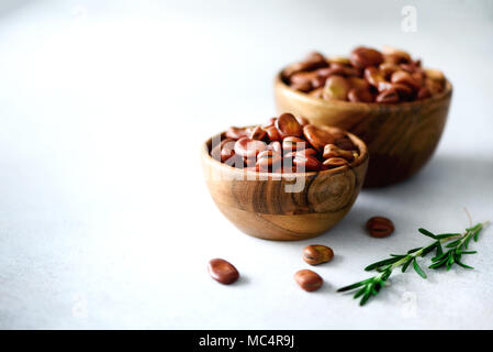 Fase organica essiccata fave in ciotole di legno e rosmarino sul cemento grigio Sfondo. Fava Vicia fagioli. Alimenti sani ingredienti. Spazio di copia Foto Stock