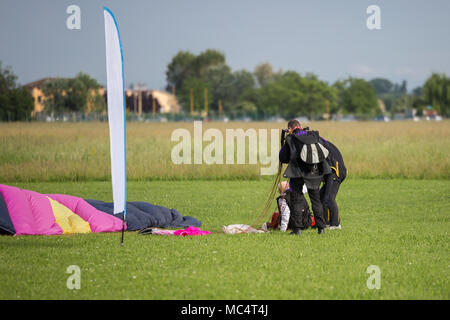 Istruttori aiutano Parachutist vecchio uomo sulla terra dopo il lancio. Foto Stock