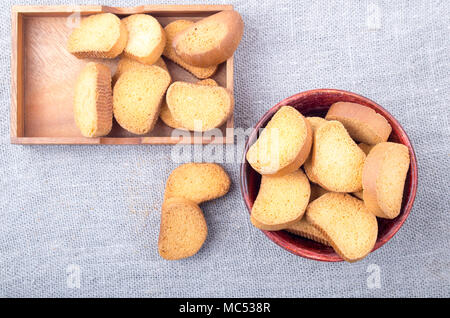Vista dall'alto su fette di pane secco in un vecchio legno bruno piatti sul grigio di una tovaglia di tela ruvida. Foto Stock