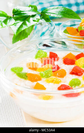 Farina di avena con colorata frutta candita in una ciotola di vetro sul tavolo per una sana colazione con profondità di campo Foto Stock