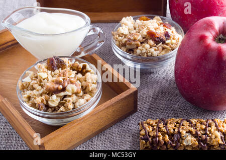 Prodotti utili per la prima colazione. Muesli con noci e uvetta, mele e yogurt su una tovaglia grigio closeup Foto Stock