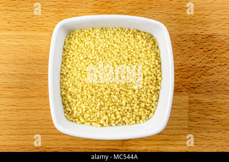 Tettuccio di colpo di couscous crudo in una ciotola bianco su uno sfondo di legno Foto Stock