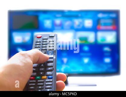 Mano, premendo sul telecomando e cambia i canali il pollice sul blu sullo schermo TV Foto Stock