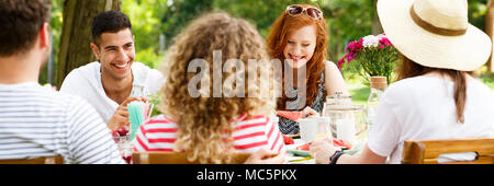 Panorama di sorridere gli amici sorseggiando un party in giardino durante la primavera soleggiata meteo