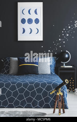 Telescopio accanto a navy blue bed contro la parete scura con stelle adesivi e poster in camera da letto interno Foto Stock