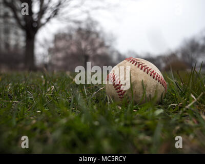 Close up sports immagine di sfondo di un vecchio usato weathered cuoio palla da baseball che stabilisce nell'erba al di fuori del campo Mostra intricati dettagli e texture Foto Stock