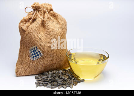 Piccolo sacchetto di tela ruvida con semi di girasole e di una ciotola di vetro con olio su uno sfondo bianco. Foto Stock