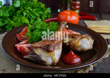 L'oca arrosto gamba, salsa, le erbe aromatiche e i pomodori in un vaso di argilla su sfondo di legno Foto Stock