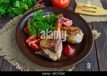 L'oca arrosto gamba, salsa, le erbe aromatiche e i pomodori in un vaso di argilla su sfondo di legno Foto Stock