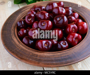 Mature amarene in un vaso di argilla su una luce sullo sfondo di legno. Close-up. Foto Stock