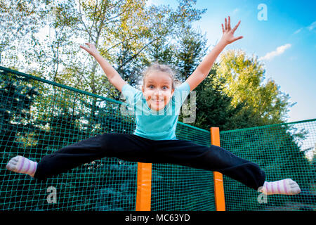 Felice ragazza caucasica del salto in alto su un trampolino su una soleggiata giornata all'aperto. Foto Stock