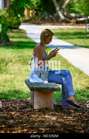 Giovani dai capelli biondi donna caucasica siede utilizzando il suo telefono nel Museo Ringling giardini in Sarasota FL, Stati Uniti d'America Foto Stock