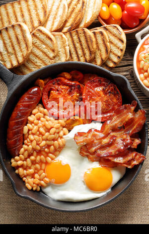 Prima colazione inglese con salsicce, pomodori grigliati, uova, bacon e fagioli in padella. Foto Stock