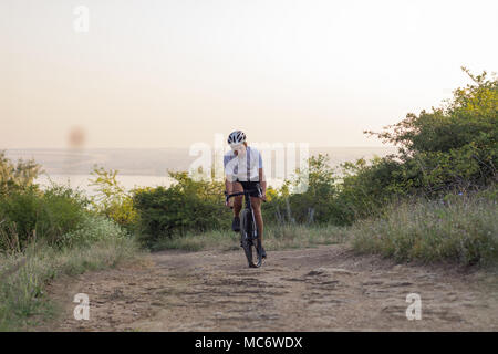 Giovane uomo nel casco con bicicletta da ciclocross che posano su per la collina e il bellissimo lago sullo sfondo Foto Stock