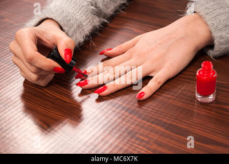 La donna la sua pittura chiodi sul dito di colore rosso sulla scrivania in legno Foto Stock