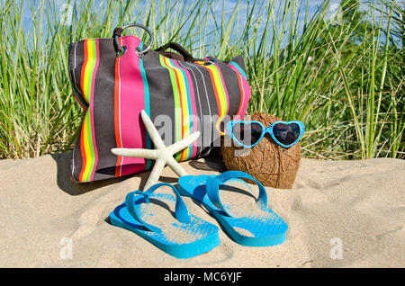 Noce di cocco con occhiali da sole e striato borsa da spiaggia in sabbia con stelle marine e flip-flop Foto Stock