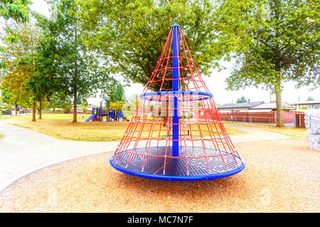 Parco giochi per bambini nel parco della città con una piramide giostra una collina nella forma di una casa, alberi e case in background Foto Stock