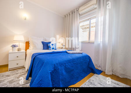 Un elegante camera da letto disposte in bianco e blu con accendere le luci e fiori sul letto mensole Foto Stock