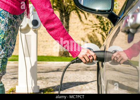 Tappi di donna auto elettrica alla stazione di carica in clima caldo Foto Stock