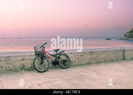 Lonely bicicletta con cestello di metallo in piedi sul molo di cemento. Seascape sfondo con barche di pescatori sulla linea di orizzonte. Tonica immagine. Foto Stock