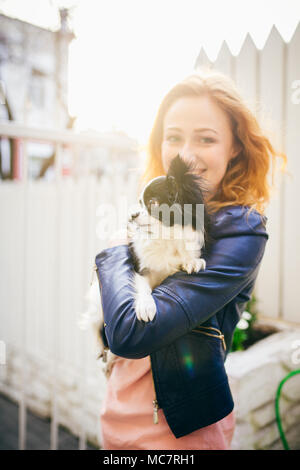 Un rosso giovane con capelli donna caucasica detiene un piccolo cane divertente nei bracci di due colori di bianco e nero chihuahua. Baci e abbracci amore mostra contro Foto Stock