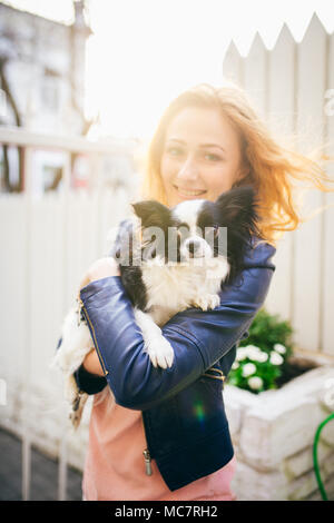 Un rosso giovane con capelli donna caucasica detiene un piccolo cane divertente nei bracci di due colori di bianco e nero chihuahua. Baci e abbracci amore mostra contro Foto Stock