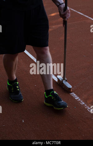 Uomo in pantaloncini corti di tennis di pulizia linee corte con una scopa Foto Stock