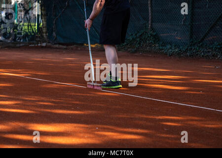 Uomo in pantaloncini corti di tennis di pulizia linee corte con una scopa Foto Stock