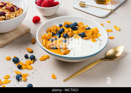 Una sana prima colazione. Fiocchi di mais con yogurt, mandorle, mirtilli e lamponi e semi di Chia. Servite con lo sciroppo di acero, muesli con mirtilli rossi secchi. Foto Stock