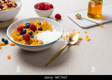 Una sana prima colazione. Fiocchi di mais con yogurt, mandorle, mirtilli e lamponi e semi di Chia. Servite con lo sciroppo di acero, muesli con mirtilli rossi secchi. Foto Stock