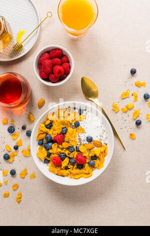 Vista dall'alto di una sana prima colazione. Fiocchi di mais con yogurt, mandorle, mirtilli e lamponi e semi di Chia. Servite con lo sciroppo di acero e succhi di frutta. Foto Stock