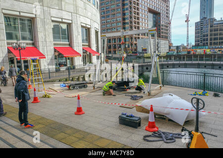 West India Quay, London, Regno Unito - 26 Marzo 2017: operai in alta viz giacche il sollevamento di una grande pietra accanto alla parte anteriore dell'acqua. Foto Stock