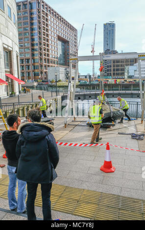 West India Quay, London, Regno Unito - 26 Marzo 2017: operai in alta viz giacche il sollevamento di una grande pietra accanto alla parte anteriore dell'acqua. Foto Stock