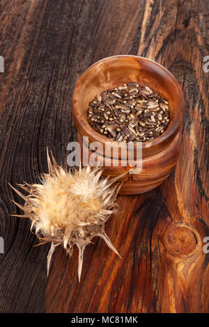 Essiccato Silybum marianum, noto come Cardo fiore e semi in ciotola di legno su un tavolo di legno. Foto Stock