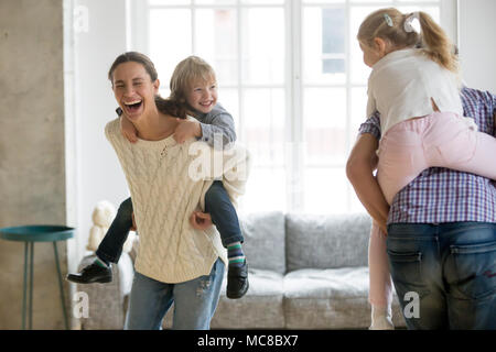 Felice madre ridere piggybacking piccolo figlio di giocare con la famiglia a casa, allegro i genitori che trasportano bambini sul retro per divertirsi insieme ai bambini un ragazzo Foto Stock