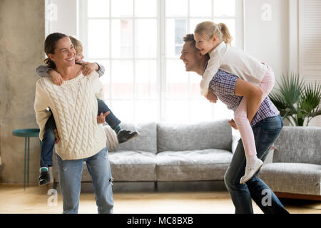 Ridere i genitori tenendo i bambini sulla schiena per bambini piggyback ride giocando insieme a casa, famiglia allegra godendo active divertente gioco insieme, si Foto Stock
