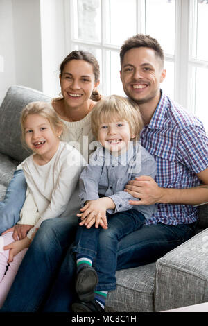 I nuovi genitori felici per due bambini adottati i fratelli concetto, sorridente giovane in posa con la figlia e il Figlio seduto sul divano insieme, allegro famiglia bonding Foto Stock