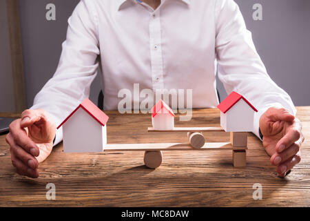 Close-up di commercianti la mano che copre l'equilibrio tra il modello di casa su altalena in Office Foto Stock